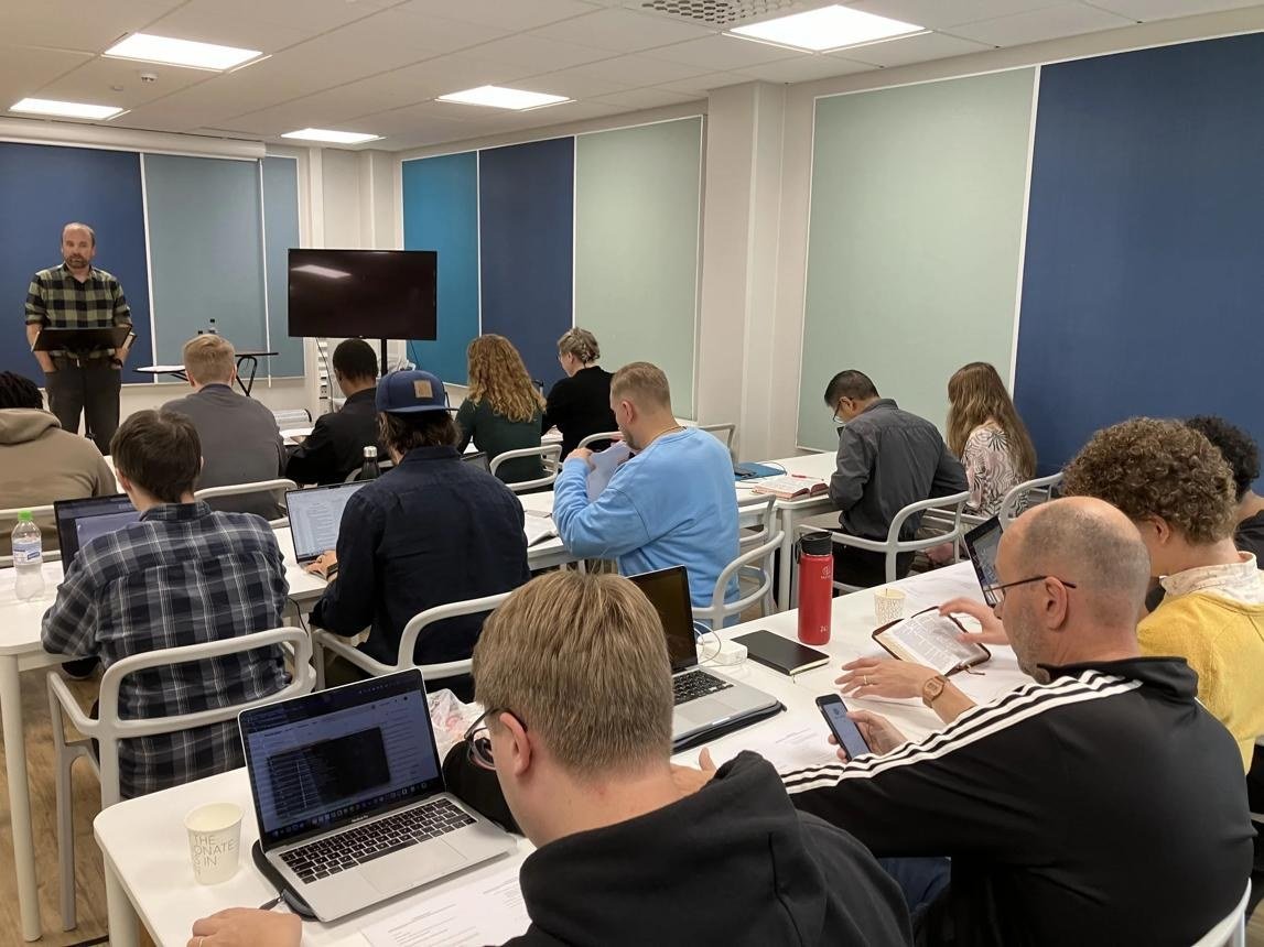 Students studying with laptops and Bibles in a classroom
